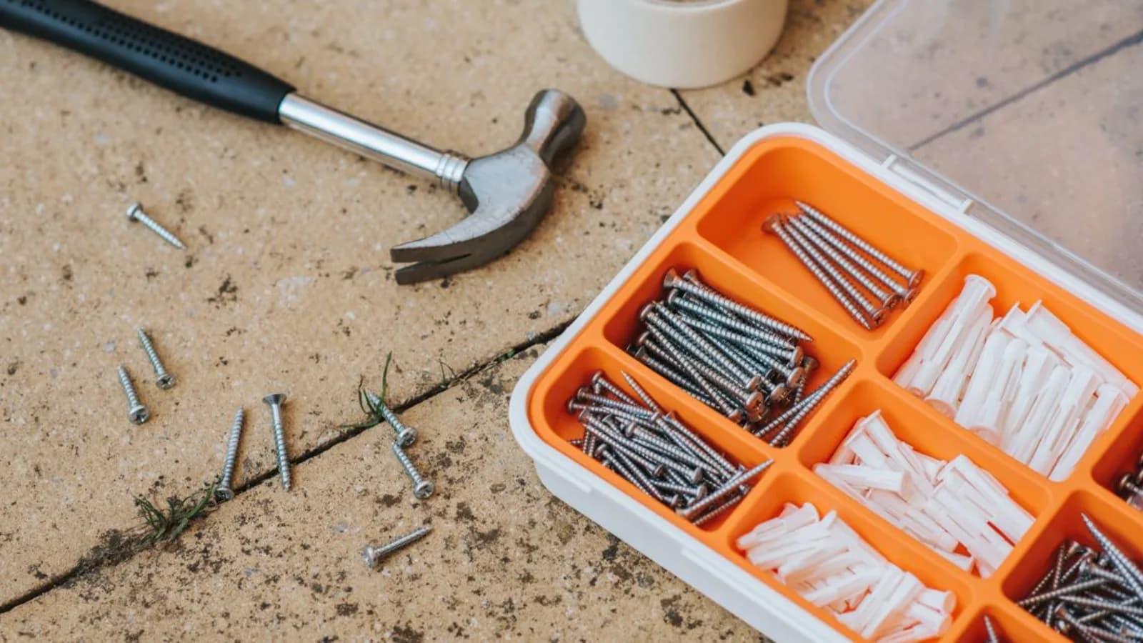 A hammer and a case of screws and wall plugs on a paved surface